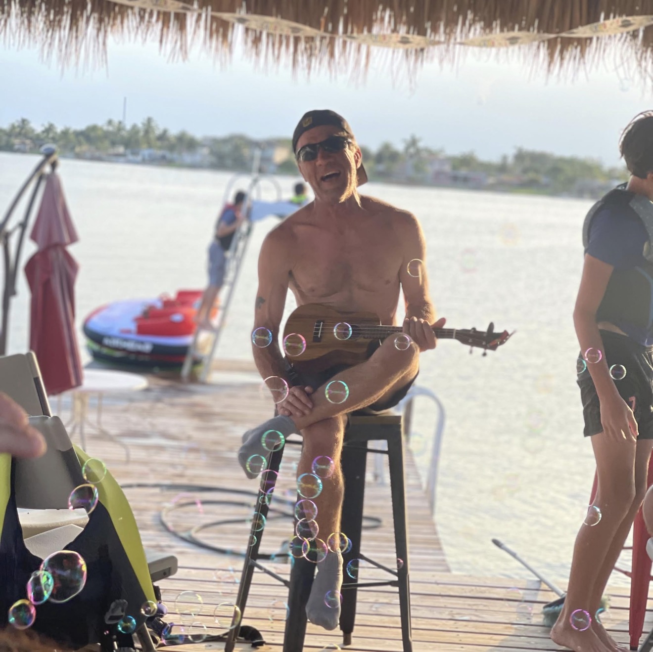 Carl Potts smiling outdoors with a ukulele beside the water